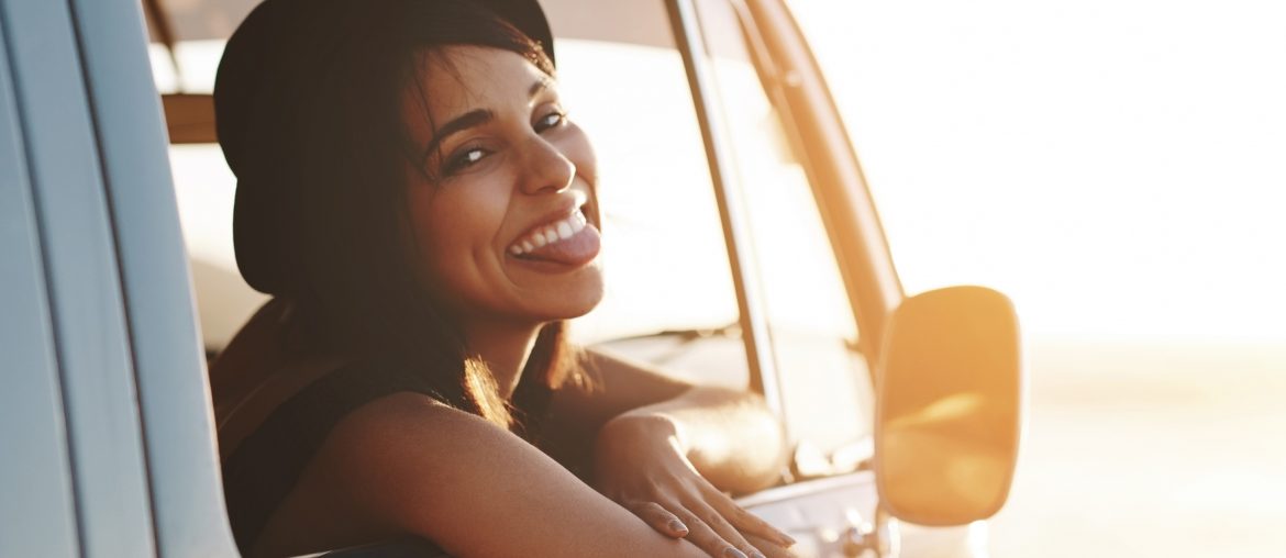 Attraktive junge Frau sitzt im Auto und bleckt die Zunge